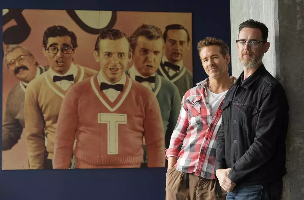 Colin Hanks, right, director of the documentary film "John Candy: I Like Me," poses for a portrait with producer Ryan Reynolds in front of a photograph of Second City comedy performers including John Candy, far left, to promote the film during the Toronto International Film Festival on Thursday, Sept. 4, 2025, in Toronto. (AP Photo/Chris Pizzello)