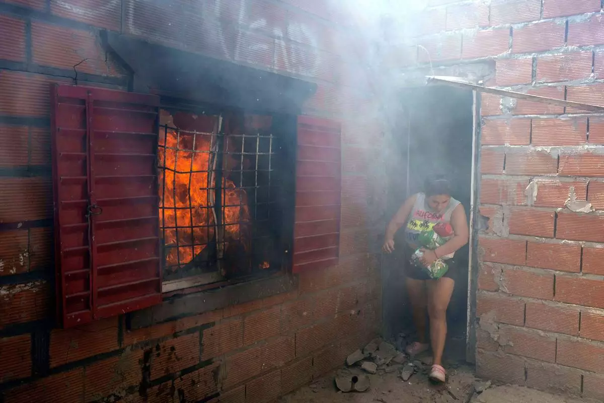 FILE PHOTO GALLERY - A woman makes off with several bags of flour as she exits the home of a suspected drug dealer, after his home was set on fire by neighbors and relatives of an 11-year-old boy who was killed during a birthday party, in Los Pumitas neighborhood of Rosario, Argentina, March 6, 2023. (AP Photo/Rodrigo Abd)