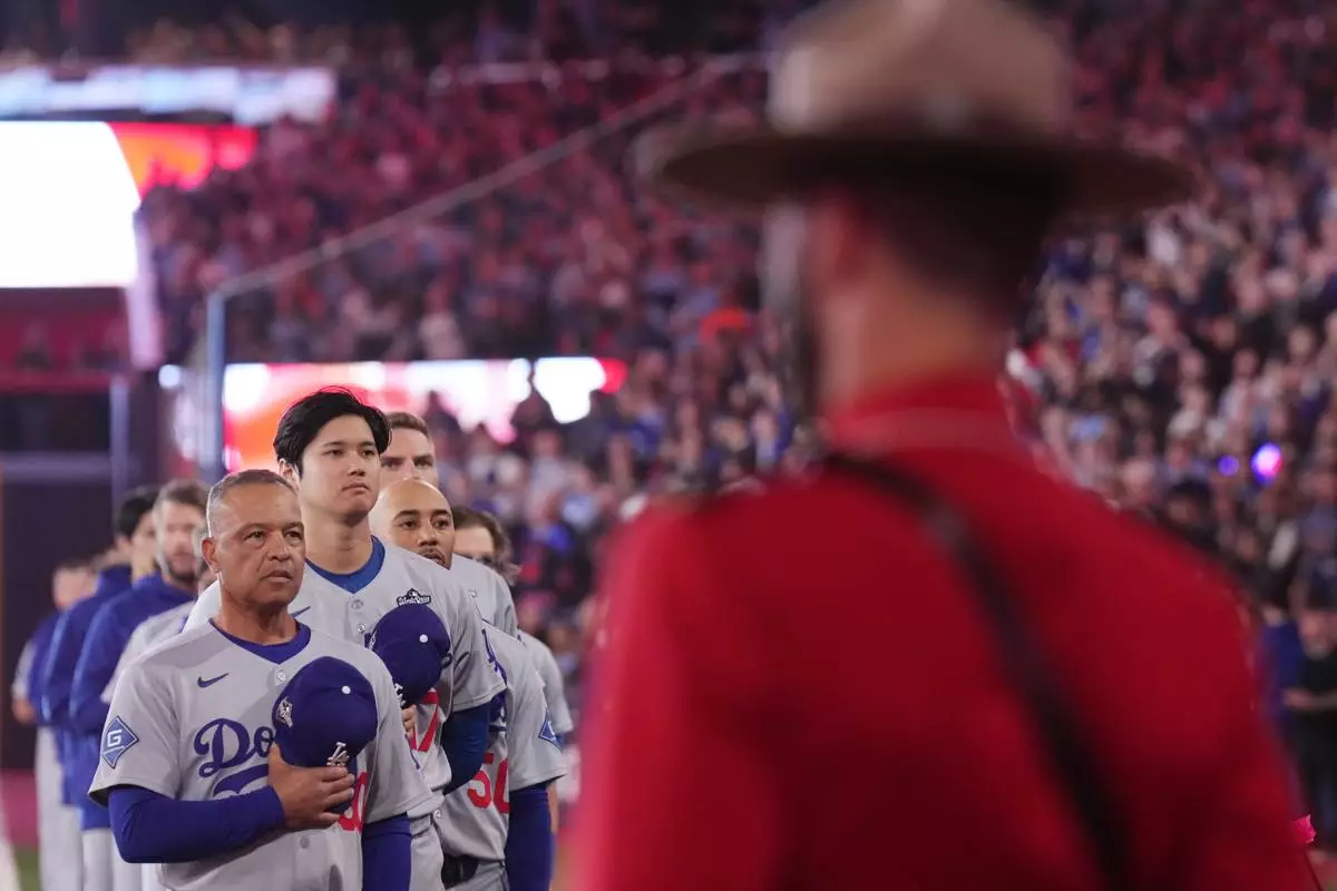 Los Angeles Dodgers manager Dave Roberts, left, two-way player Shohei Ohtani (17) and shortstop Mookie Betts (50) listen to the Canadian national anthem as Royal Canadian Mounted Police look on, ahead of the first inning Royal Canadian Mounted Police in Game 1 of baseball's World Series, Friday, Oct. 24, 2025, in Toronto. (Nathan Denette/The Canadian Press via AP)