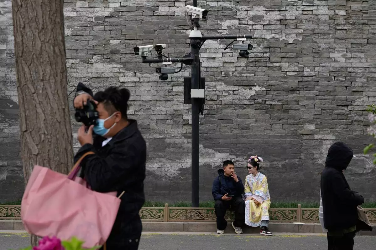 A woman in traditional Chinese clothing talks with a man underneath security cameras outside the Forbidden City in Beijing, Saturday, April 12, 2025. (AP Photo/Ng Han Guan)
