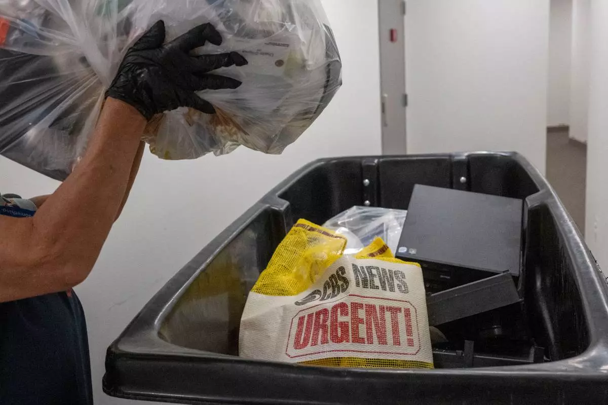 A cleaning person throws a bag of trash in a dumpster as members of the media pack up their belongings in the press area of the Pentagon, Wednesday, Oct. 15, 2025 in Washington. (AP Photo/Kevin Wolf)