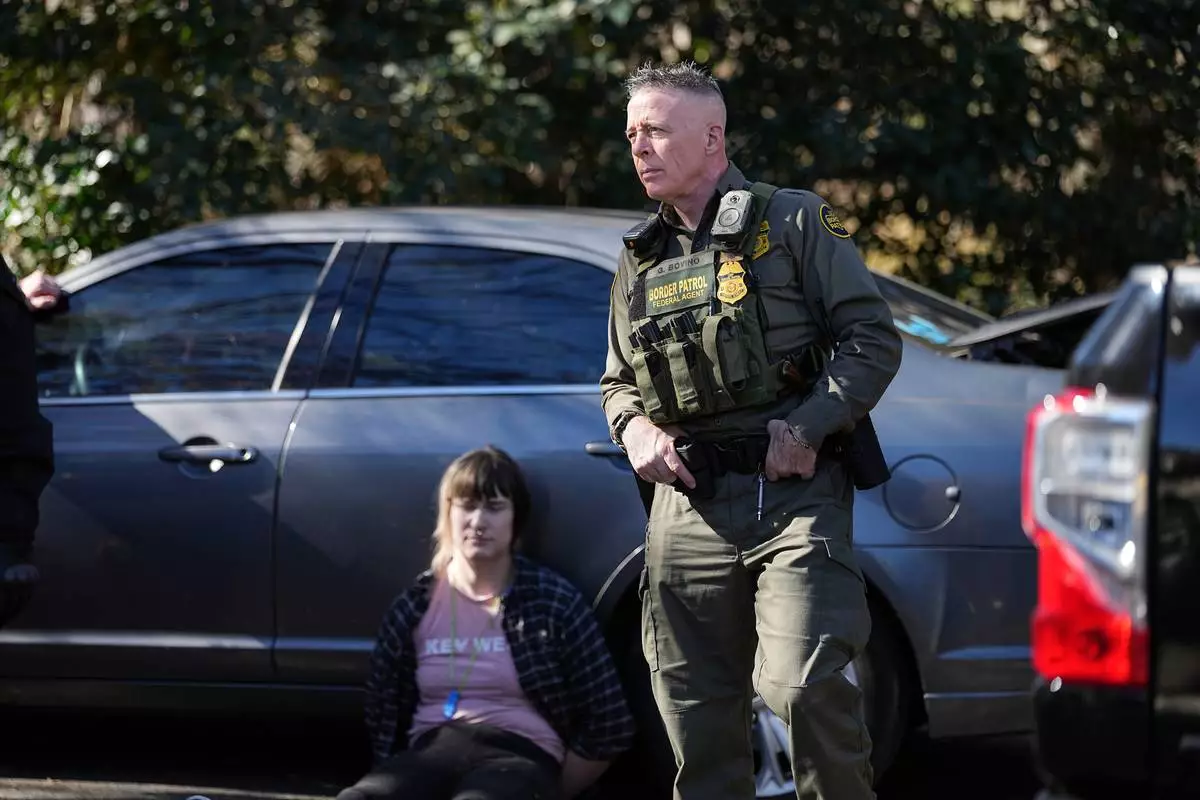 U.S. Border Patrol Commander at large Gregory Bovino, right, looks on as a detainee sits by a car, Monday, Nov. 17, 2025, in Charlotte, N.C. (AP Photo/Matt Kelley)