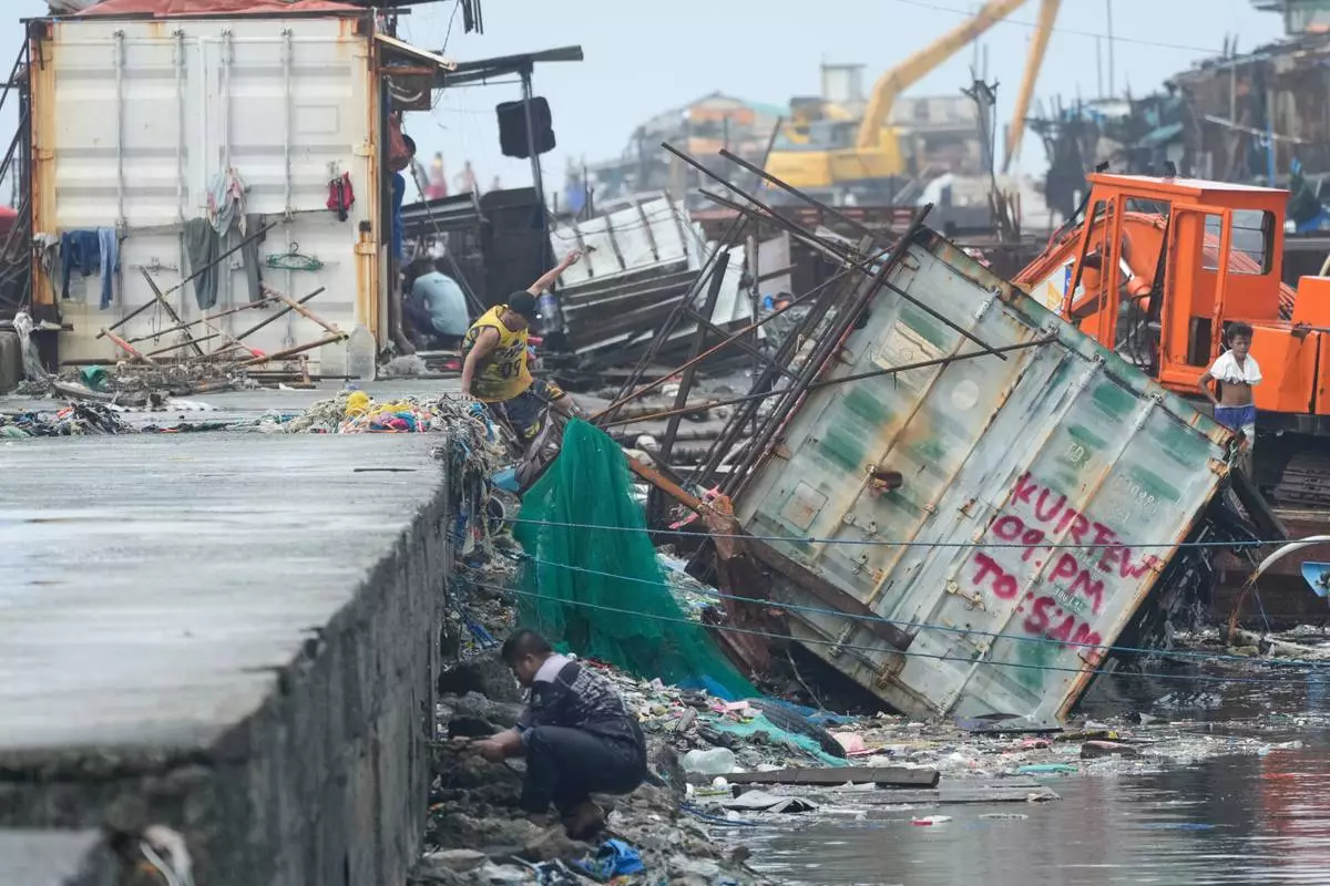 A man jumps beside a container van that was toppled due to Typhoon Fung-wong on Monday, Nov. 10, 2025, in Navotas, Philippines. (AP Photo/Aaron Favila)