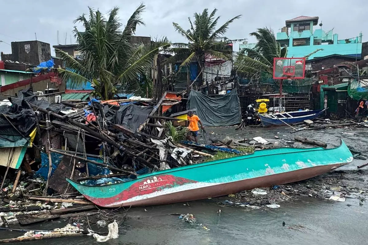 A man walks beside a damaged house and boat due to Typhoon Fung-wong along a coastal village on Monday, Nov. 10, 2025, in Navotas, Philippines. (AP Photo/Aaron Favila)