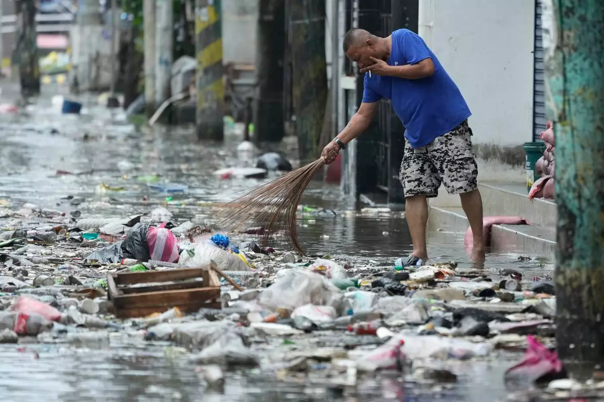 A man cleans garbage along a flooded street due to Typhoon Fung-wong and high tide on Monday, Nov. 10, 2025, in Navotas, Philippines. (AP Photo/Aaron Favila)