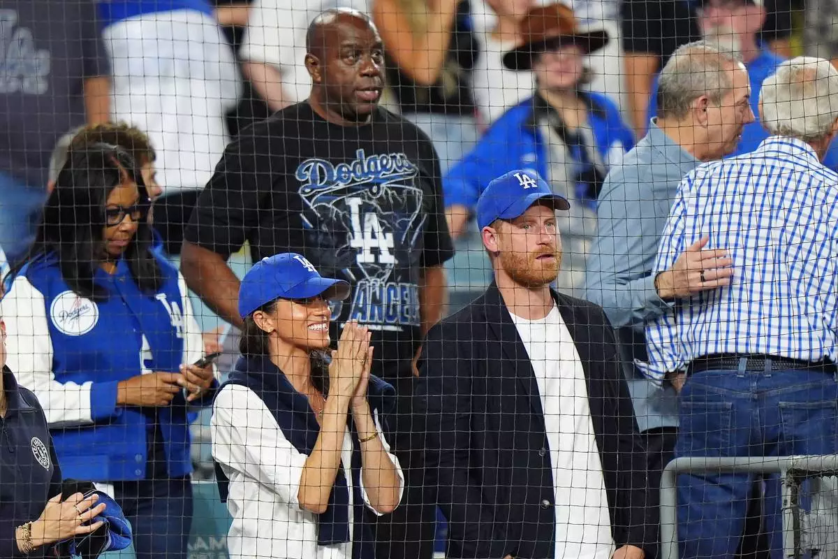 Prince Harry, right, and Meghan Markle, left, The Duke and Duchess of Sussex, and Magic Johnson, back, watch during the seventh inning in Game 4 of baseball's World Series between the Los Angeles Dodgers and the Toronto Blue Jays in Los Angeles, Tuesday, Oct. 28, 2025. (Frank Gunn/The Canadian Press via AP)