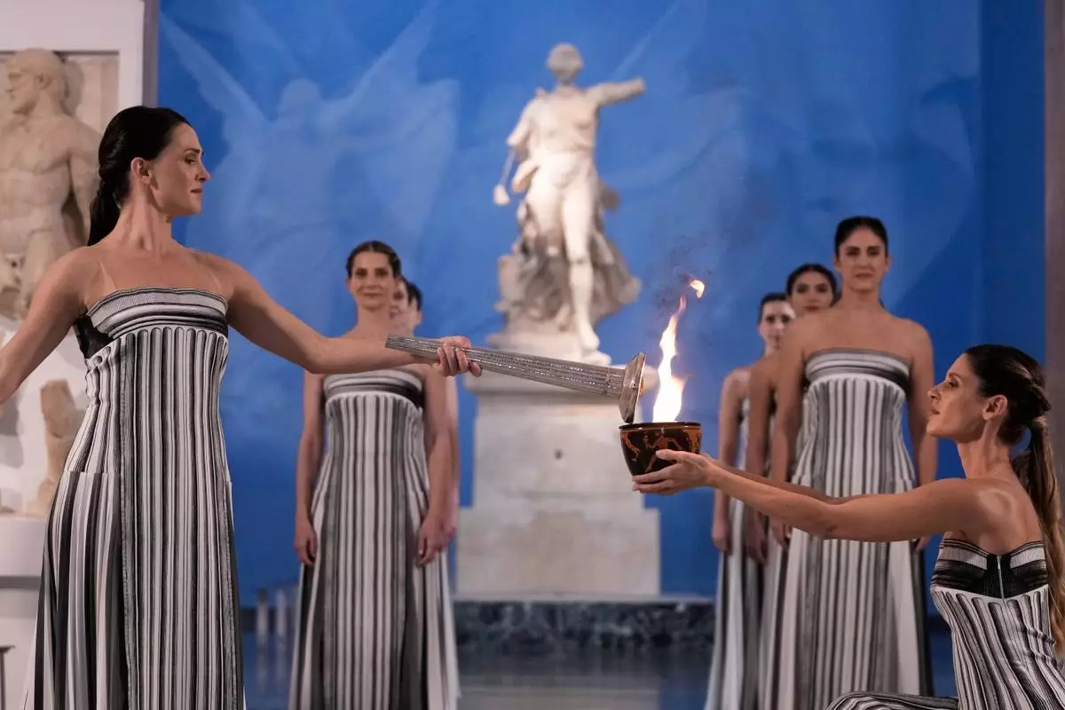 High Priestess Mary Mina, left, lights a torch from the Olympic flame during the flame lighting ceremony for the Milan Cortina 2026 Winter Olympics, at the archaeological museum of Olympia, Greece, Wednesday, Nov. 26, 2025. (AP Photo/Thanassis Stavrakis)