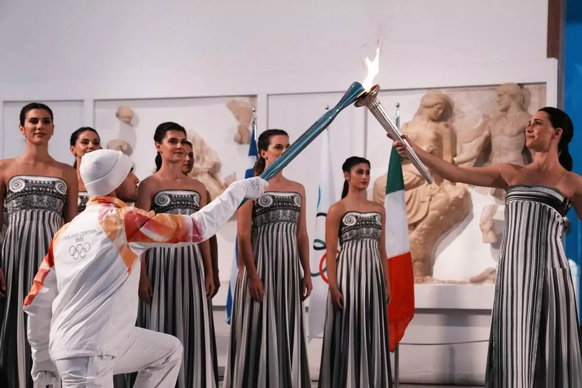 Actress Mary Mina, right, playing the role of high priestess, passes the Olympic flame to the first torchbearer Greek rower Petros Gaidatzis, during the flame lighting ceremony for the Milan Cortina 2026 Winter Olympics, at the archaeological museum of Olympia, Greece, Wednesday, Nov. 26, 2025. (AP Photo/Thanassis Stavrakis)
