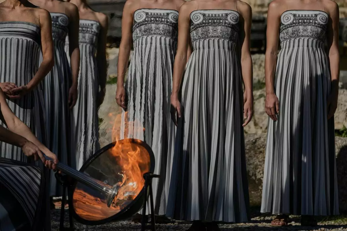 Actress Mary Mina, playing a priestess, lights the flame during a rehearsal ahead of the flame lighting for the Milan Cortina 2026 Winter Olympics, at the Ancient Olympia site, Greece, Monday, Nov. 24, 2025. (AP Photo/Petros Giannakouris)