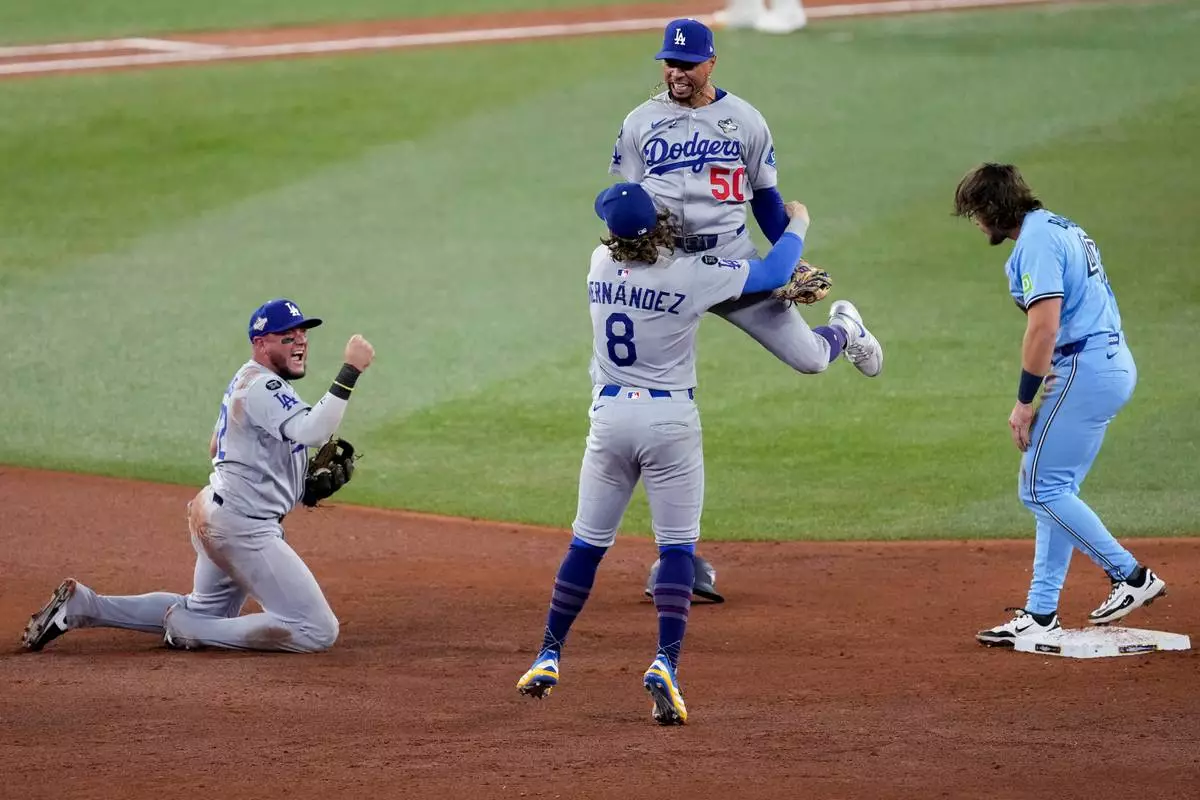 Los Angeles Dodgers' Mookie Betts (50) leaps into the arms of Kiké Hernández (8) as Miguel Rojas, left, pumps his fist after Toronto Blue Jays' Addison Barger, right, was forced out to end Game 6 of baseball's World Series, Friday, Oct. 31, 2025, in Toronto. (AP Photo/Ashley Landis)