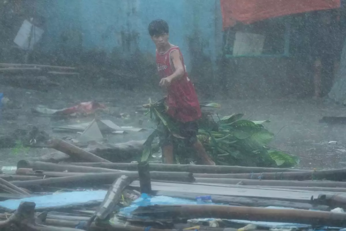 A resident cleans up debris during heavy rainfall in their coastal village, which was affected by Typhoon Fung-wong on Monday, Nov. 10, 2025, in Navotas, Philippines. (AP Photo/Aaron Favila)