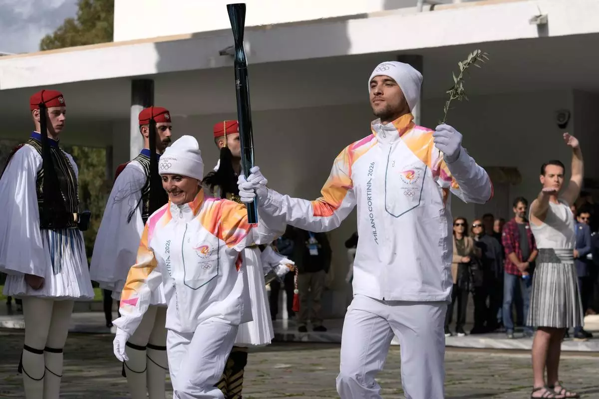 Greek rower Petros Gaidatzis, right, and former Italy's Cross Country skier Stefania Belmondo start the torch relay after the ceremony of the flame lighting for the Milan Cortina 2026 Winter Olympics, at the archaeological museum of Olympia, Greece, Wednesday, Nov. 26, 2025. (AP Photo/Petros Giannakouris)