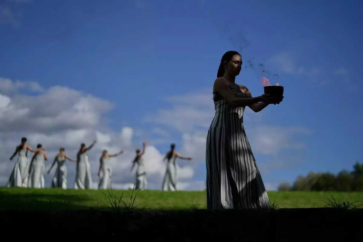 Actress Mary Mina, playing the high priestess holds a pot with the flame during a rehearsal ahead of the flame lighting for the Milan Cortina 2026 Winter Olympics, at the Ancient Olympia site, Greece, Monday, Nov. 24, 2025. (AP Photo/Petros Giannakouris)