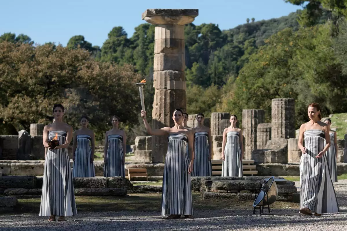 Actress Mary Mina, center, playing the role of high priestess holds the torch with the flame during a rehearsal ahead of the flame lighting for the Milan Cortina 2026 Winter Olympics, at the Ancient Olympia site, Greece, Monday, Nov. 24, 2025. (AP Photo/Thanassis Stavrakis)