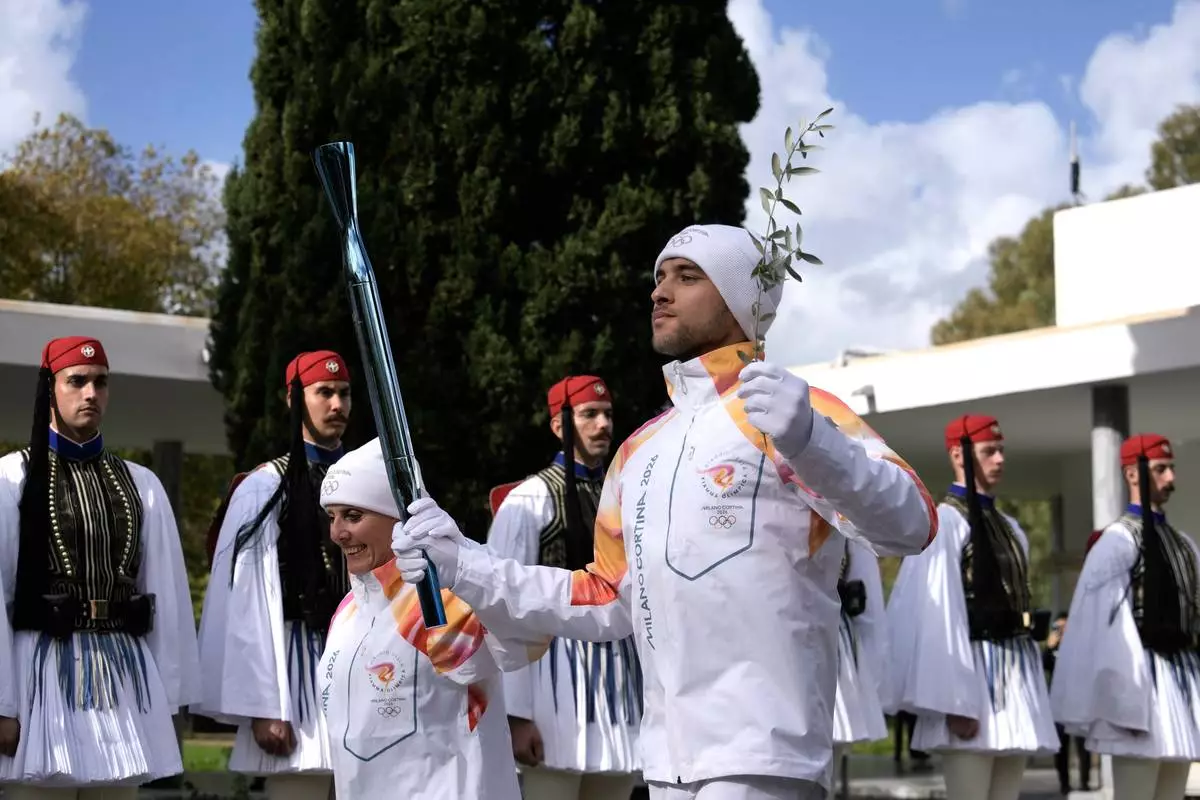 Greek rower Petros Gaidatzis, right, and former Italy's Cross Country skier Stefania Belmondo start the torch relay after the ceremony of the flame lighting for the Milan Cortina 2026 Winter Olympics, at the archaeological museum of Olympia, Greece, Wednesday, Nov. 26, 2025. (AP Photo/Petros Giannakouris)
