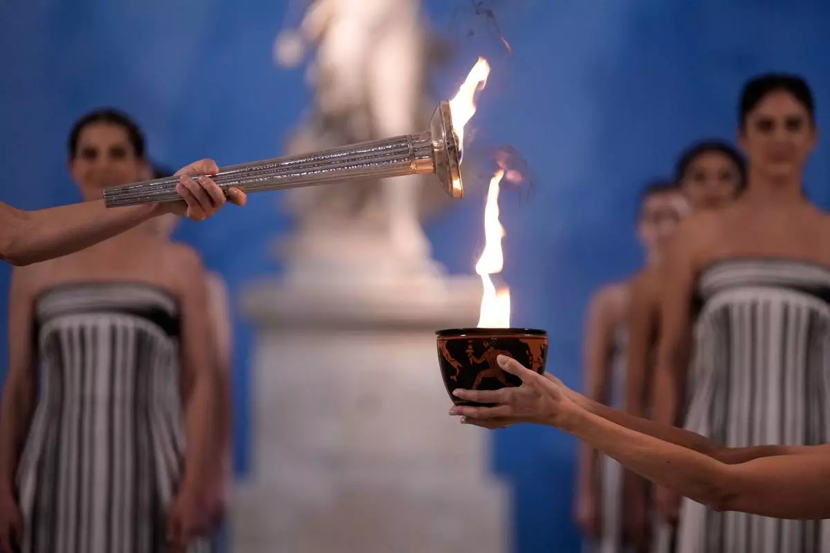 High Priestess Mary Mina, left, lights a torch from the Olympic flame during the flame lighting ceremony for the Milan Cortina 2026 Winter Olympics, at the archaeological museum of Olympia, Greece, Wednesday, Nov. 26, 2025. (AP Photo/Thanassis Stavrakis)