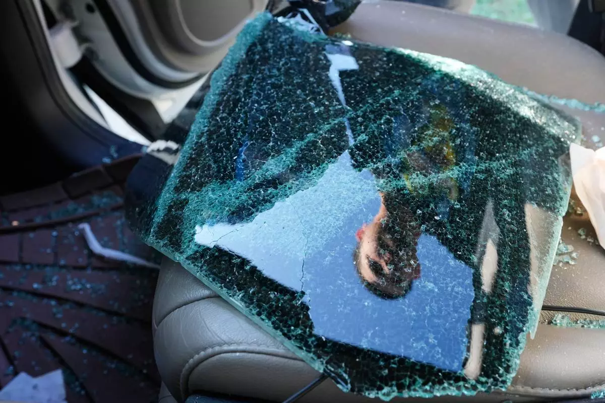 Jonathan Escalante stands over the broken window of his mother's car, which was shattered by federal immigration agents who took her away, during a federal immigration crackdown in Kenner, La., Tuesday, Dec. 9, 2025. (AP Photo/Gerald Herbert)