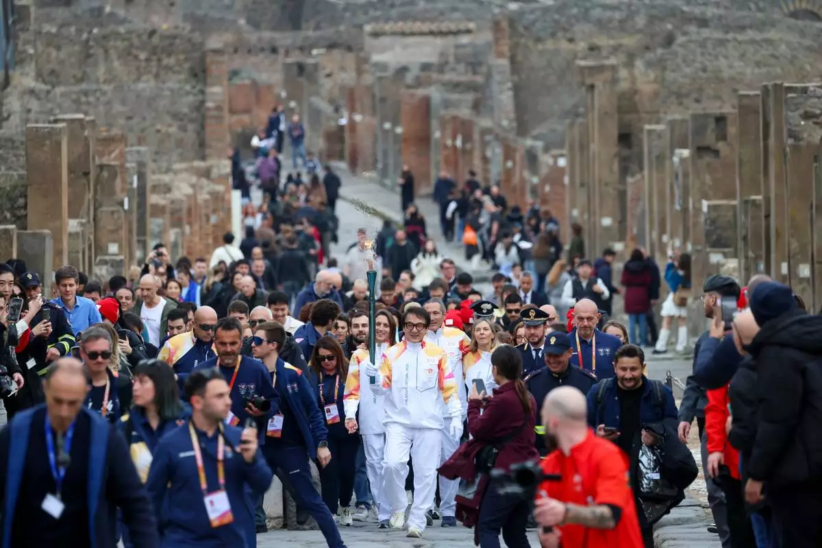 Actor Jackie Chan holds the olympic torch passing through the Archaeological Park in Pompeii, Italy, Monday, Dec. 22, 2025. (Alessandro Garofalo/LaPresse via AP)