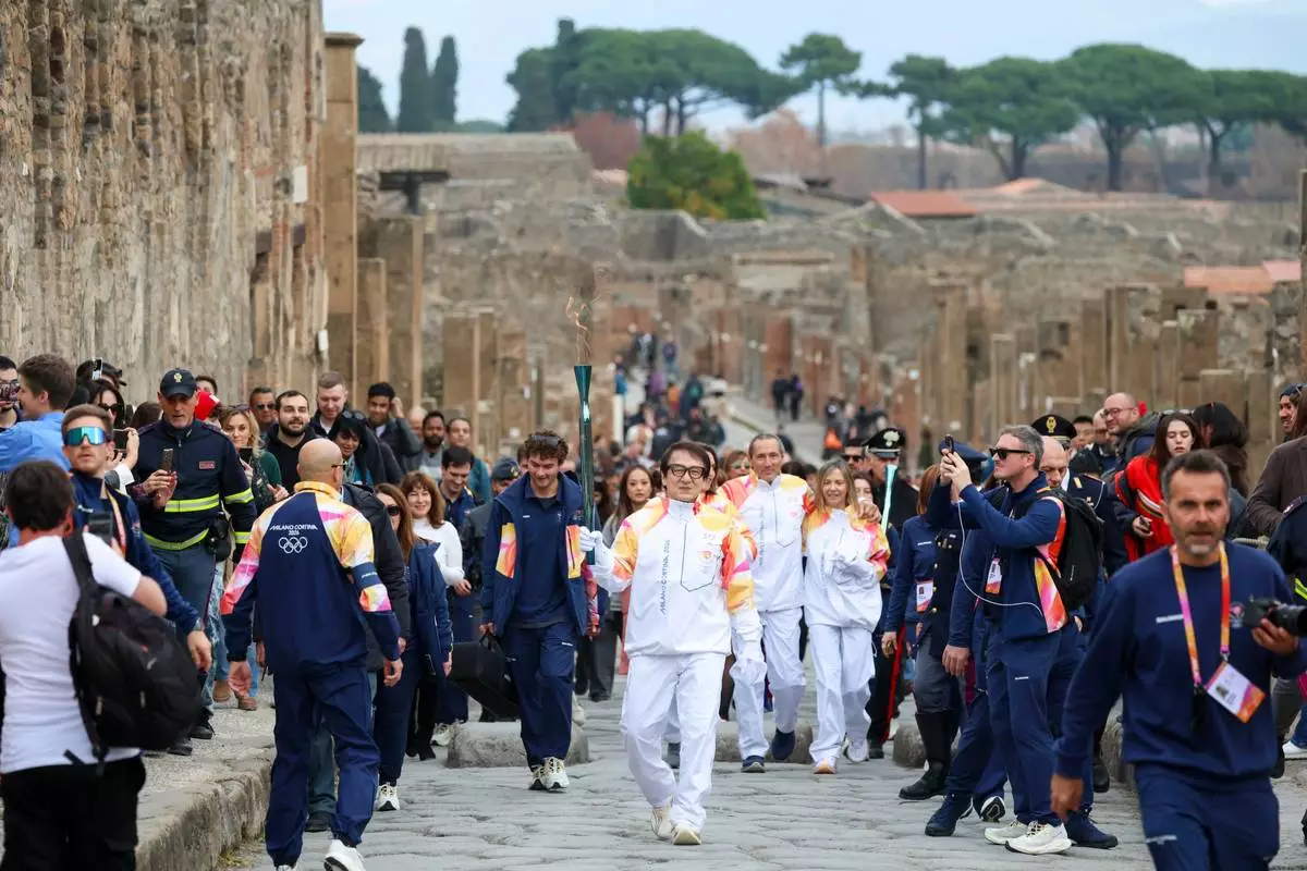 Actor Jackie Chan holds the olympic torch passing through the Archaeological Park in Pompeii, Italy, Monday, Dec. 22, 2025. (Alessandro Garofalo/LaPresse via AP)