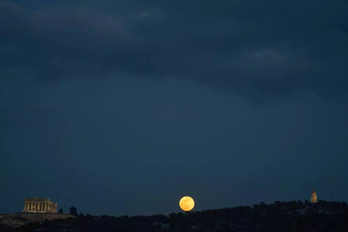 The snow moon rises behind Philopappos Hill, between the Parthenon, left, and the Philopappos Monument, right, in Athens, Greece, on Feb. 12, 2025. (AP Photo/Petros Giannakouris, File)