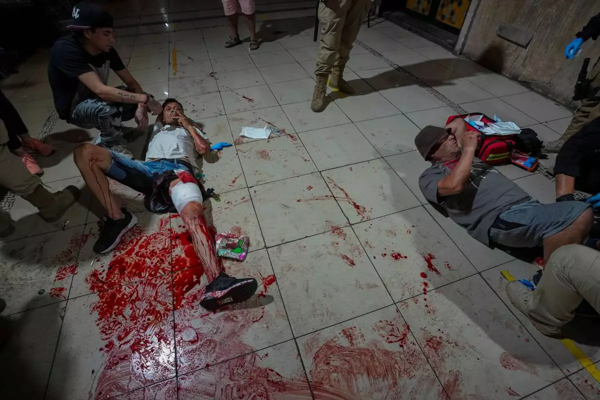 FILE - A man wounded in a fight smokes next to his friend, also injured, while waiting for an ambulance after a fight in a shopping arcade in Santiago, Chile, Dec. 2, 2025. (AP Photo/Esteban Felix, File)
