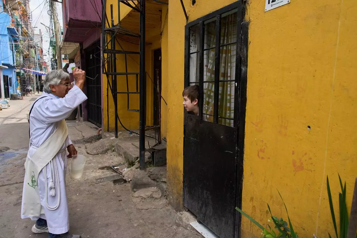 FILE - Catholic deacon Mario Rene Garcia sprinkles holy water with a blessing for Martial Martinez as he peeks out from a window during a procession celebrating the feast day of Paraguay's patroness, Our Lady of Caacupe, popularly known as the Blue Virgin, in Buenos Aires, Argentina, Dec. 8, 2025. (AP Photo/Rodrigo Abd, File)