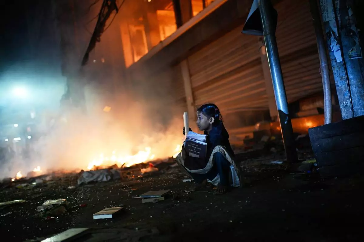 FILE - A girl rescues books from a shop near the Prothom Alo daily newspaper which was set on fire by protesters after news reached the country from Singapore of the death of a prominent activist Sharif Osman Hadi, in Dhaka, Bangladesh, Friday, Dec. 19, 2025. (AP Photo/Mahmud Hossain Opu, File)