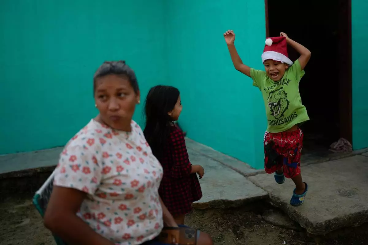 FILE - Mathias jumps after receiving a Christmas present from his mother, Mariela Gómez, left, in Maracay, Venezuela, Wednesday, Dec. 24, 2025. The two returned home after abandoning their journey to the United States following President Donald Trump's immigration crackdown. (AP Photo/Matias Delacroix, File)