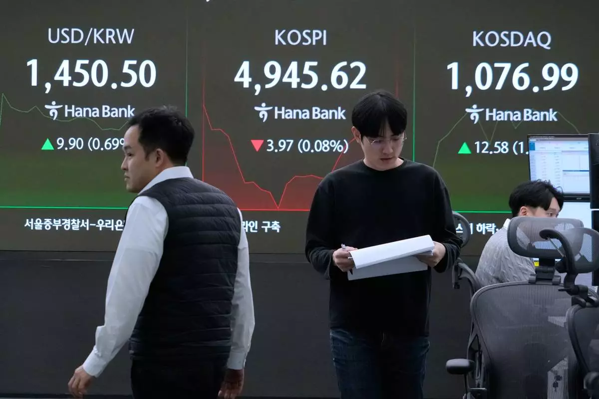 Currency traders pass by a screen showing the Korea Composite Stock Price Index (KOSPI), center, and the foreign exchange rate between U.S. dollar and South Korean won, left, at the foreign exchange dealing room of the Hana Bank headquarters in Seoul, South Korea, Tuesday, Jan. 27, 2026. (AP Photo/Ahn Young-joon)