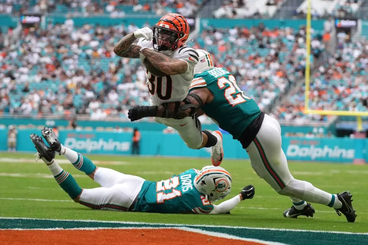 FILE - Cincinnati Bengals running back Chase Brown, center, breaks a tackle by Miami Dolphins linebacker Jordyn Brooks, right, for a touchdown during the second half of an NFL football game, Dec. 21, 2025, in Miami Gardens, Florida. (AP Photo/Lynne Sladky, File)