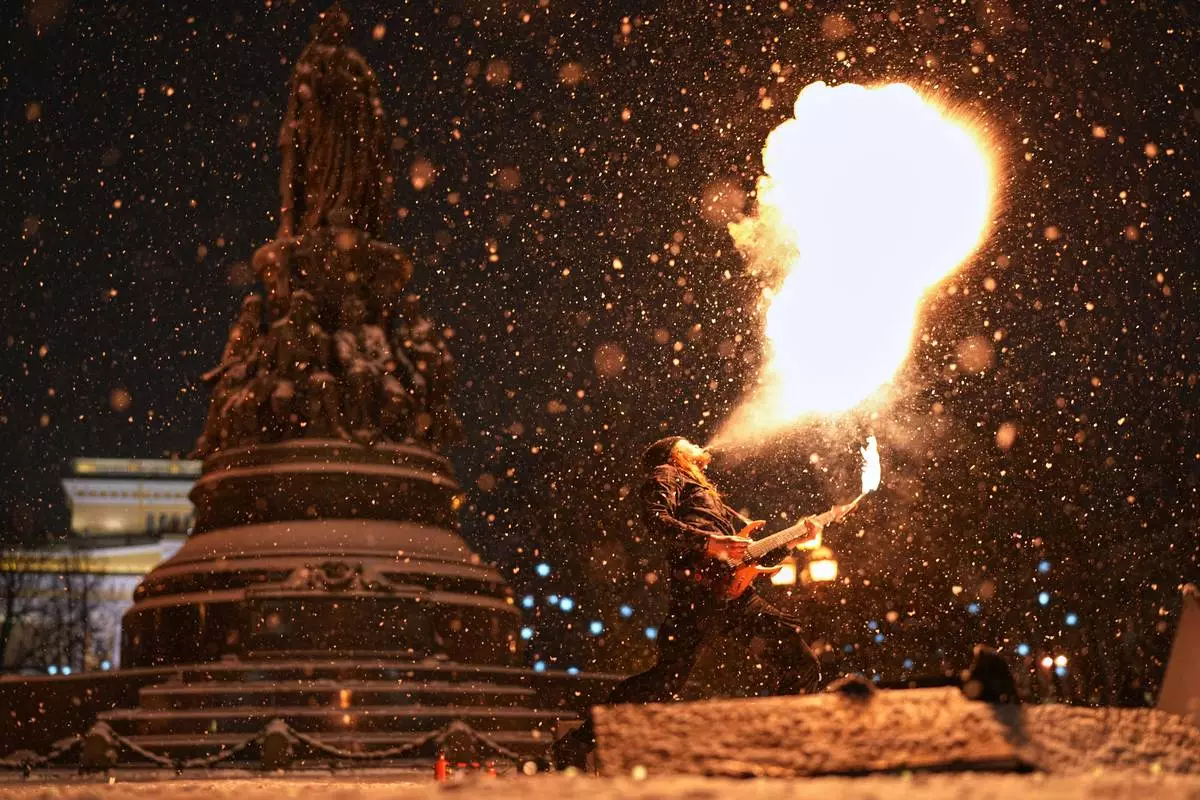 FILE - A street performer spits fire and plays a guitar in the snow in St. Petersburg, Russia, Dec. 29, 2025. (AP Photo/Dmitri Lovetsky, File)