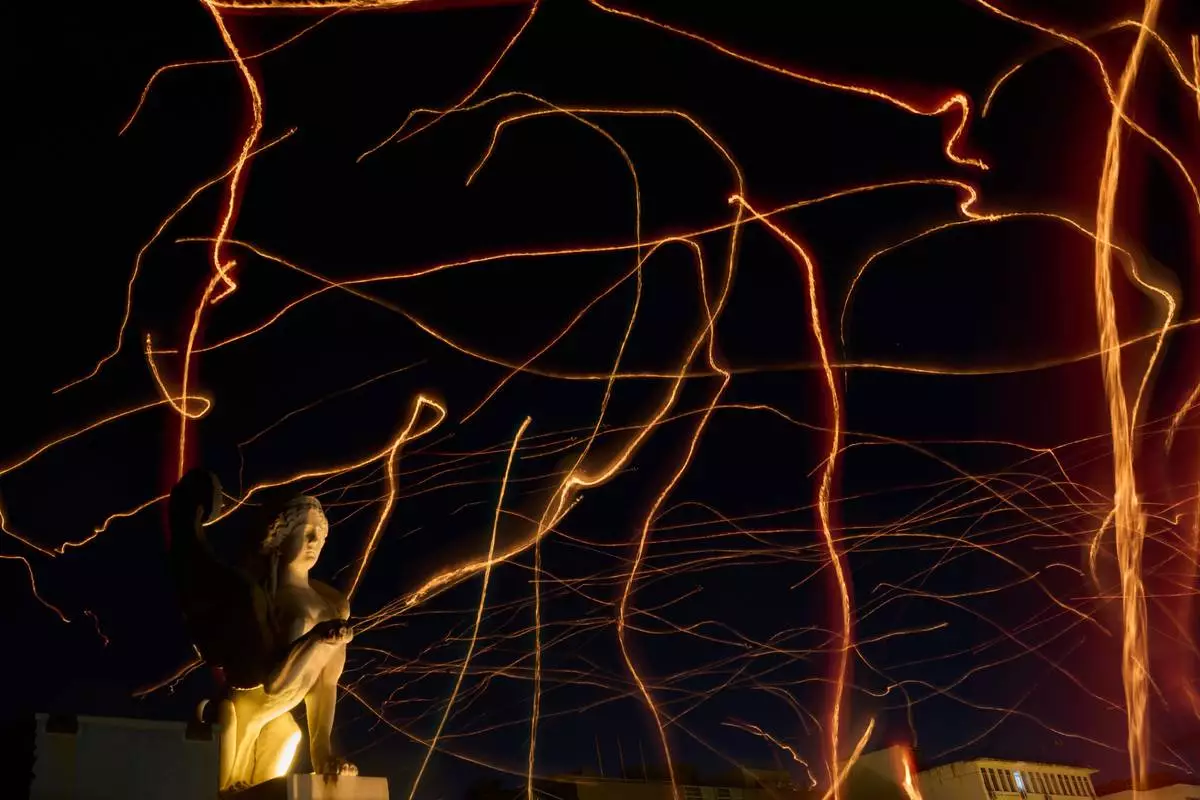FILE - This photo taken with low shutter speed shows tracers cross the sky made by floating lanterns during an event coined The night of wishes, in front of the Athens City Hall, Greece, Dec. 26, 2025. (AP Photo/Petros Giannakouris File)