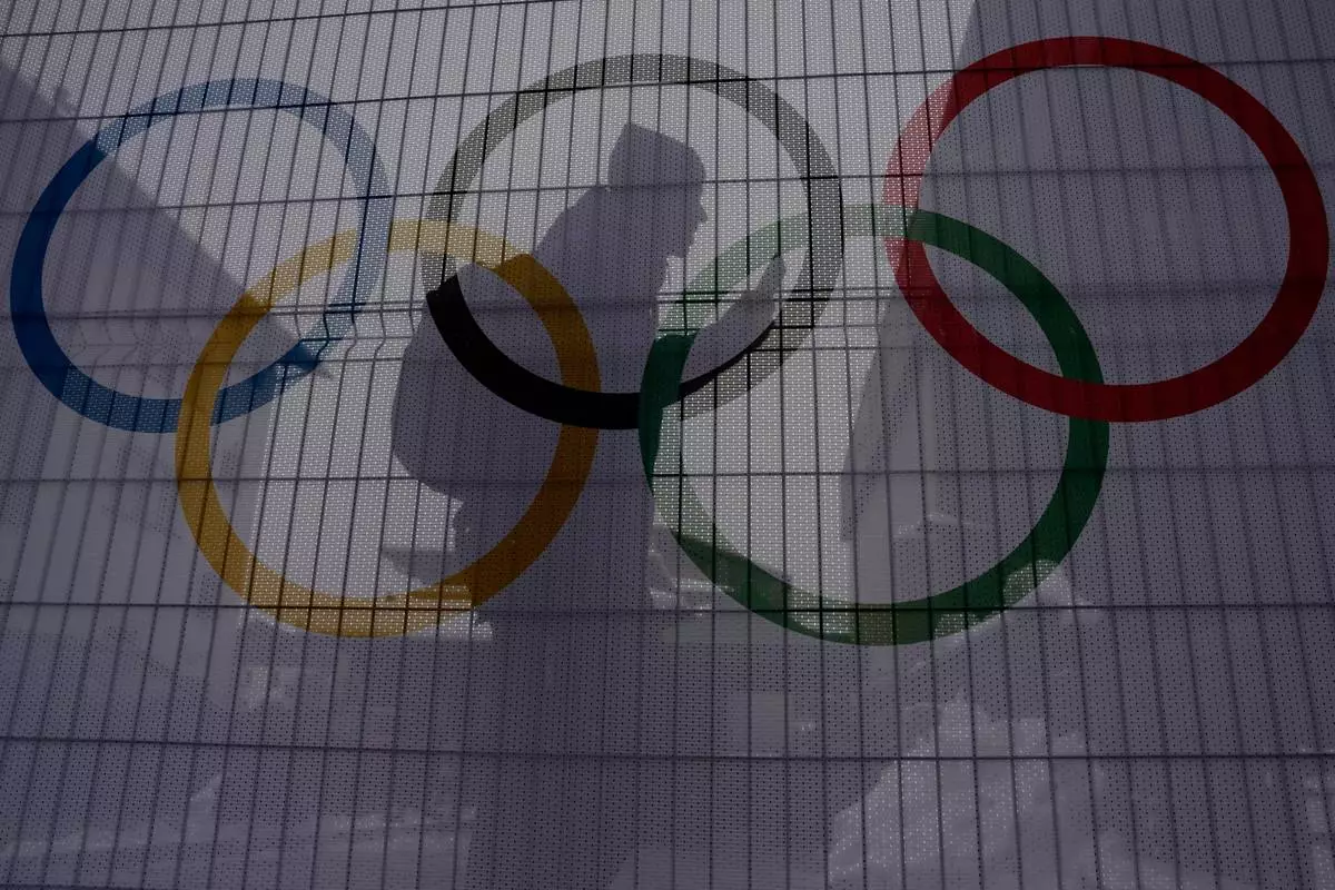 A person walks past Olympic rings on net covered fences at the 2026 Winter Olympics, in Bormio, Italy, Wednesday, Feb. 4, 2026. (AP Photo/John Locher)