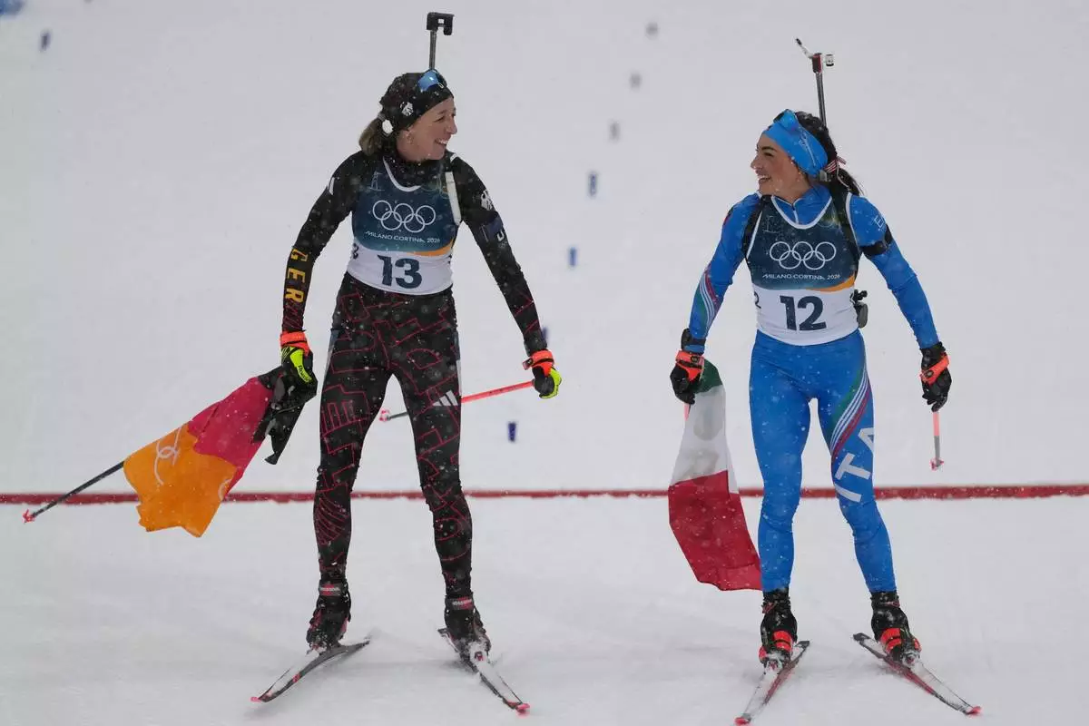 Franziska Preuss, of Germany, and Dorothea Wierer, of Italy, who both announced their retirement from the sport, celebrate after the women's 12.5-kilometer mass start biathlon race at the 2026 Winter Olympics in Anterselva, Italy, Saturday, Feb. 21, 2026. (AP Photo/Mosa'ab Elshamy)