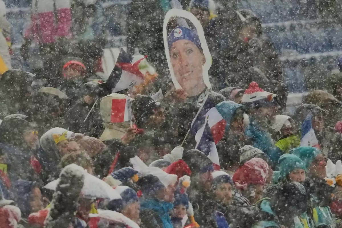 French fans hold a photo of Oceane Michelon of France the Biathlon Women's 12.5km Mass Start at the 2026 Winter Olympics, in Anterselva, Italy, Saturday, Feb. 21, 2026. (AP Photo/Christophe Ena)