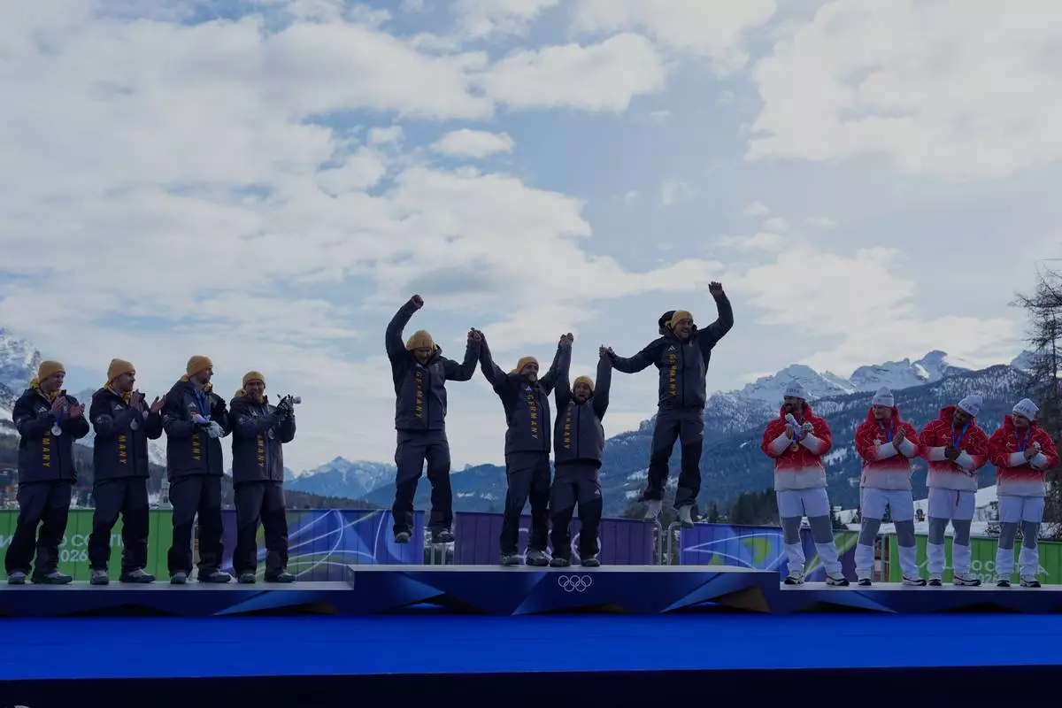 From left, Germany's silver medal team Francesco Friedrich, Matthias Sommer, Alexander Schuller and Felix Straub, Germany's gold medal team Johannes Lochner, Thorsten Margis, Jorn Wenzel and Georg Fleischauer and Switzerland's bronze medalists Michael Vogt, Andreas Haas, Amadou David Ndiaye and Mario Aeberhard take celebrate on the podium of the four man bobsled competition at the 2026 Winter Olympics, in Cortina d'Ampezzo, Italy, Sunday, Feb. 22, 2026.(AP Photo/Alessandra Tarantino)