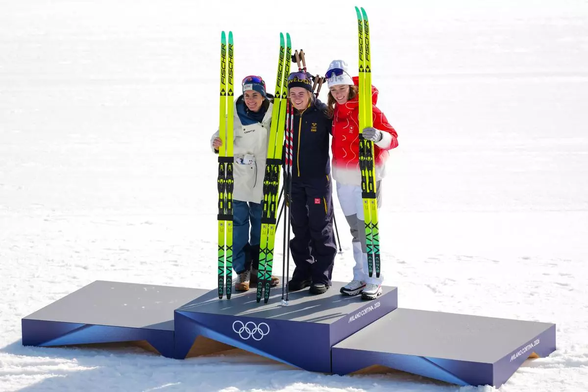 Gold medalist Ebba Andersson, of Sweden, poses on the podium flanked by silver medalist Heidi Weng, of Norway, left, and bronze medalist Nadja Kaelin, of Switzerland, after the cross country skiing women's 50km mass start classic at the 2026 Winter Olympics, in Tesero, Italy, Sunday, Feb. 22, 2026. (AP Photo/Kirsty Wigglesworth)