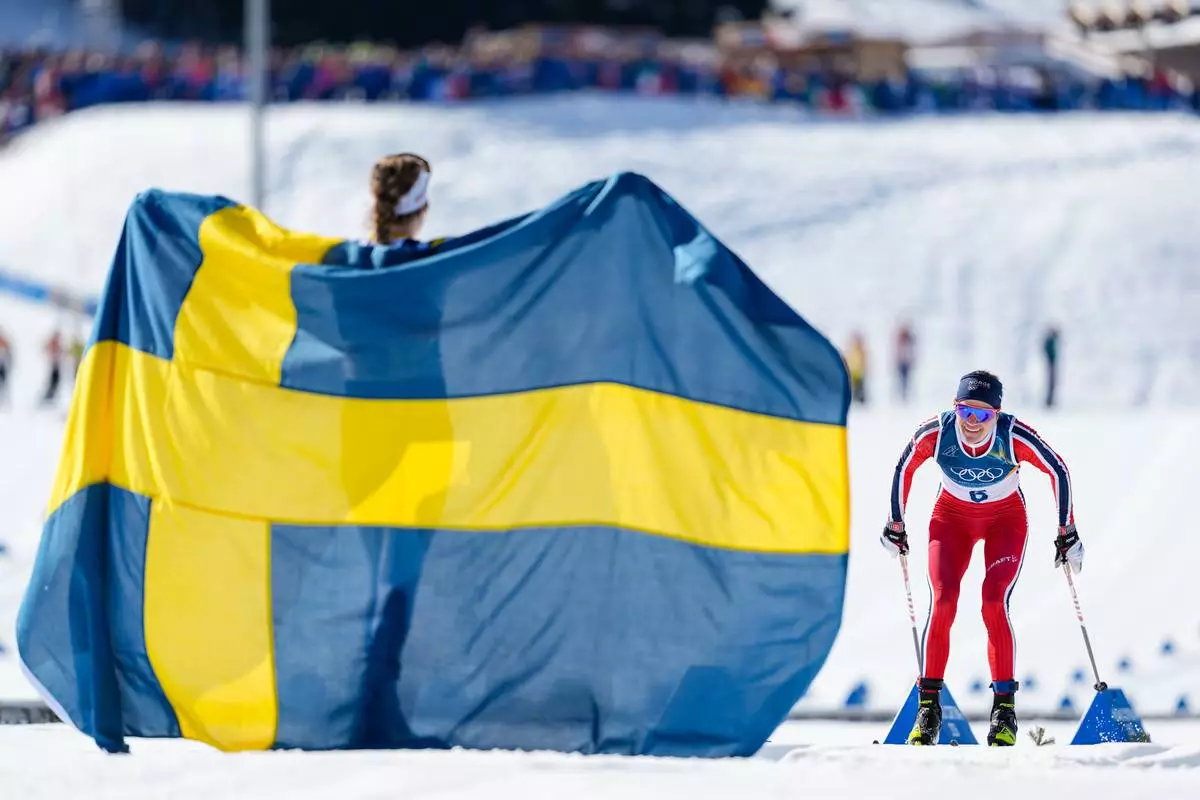 Gold medalist Ebba Andersson, of Sweden, left, watches Heidi Weng, of Norway, approach the finish line to win the silver medal in the cross country skiing women's 50km mass start classic at the 2026 Winter Olympics, in Tesero, Italy, Sunday, Feb. 22, 2026. (AP Photo/Matthias Schrader)