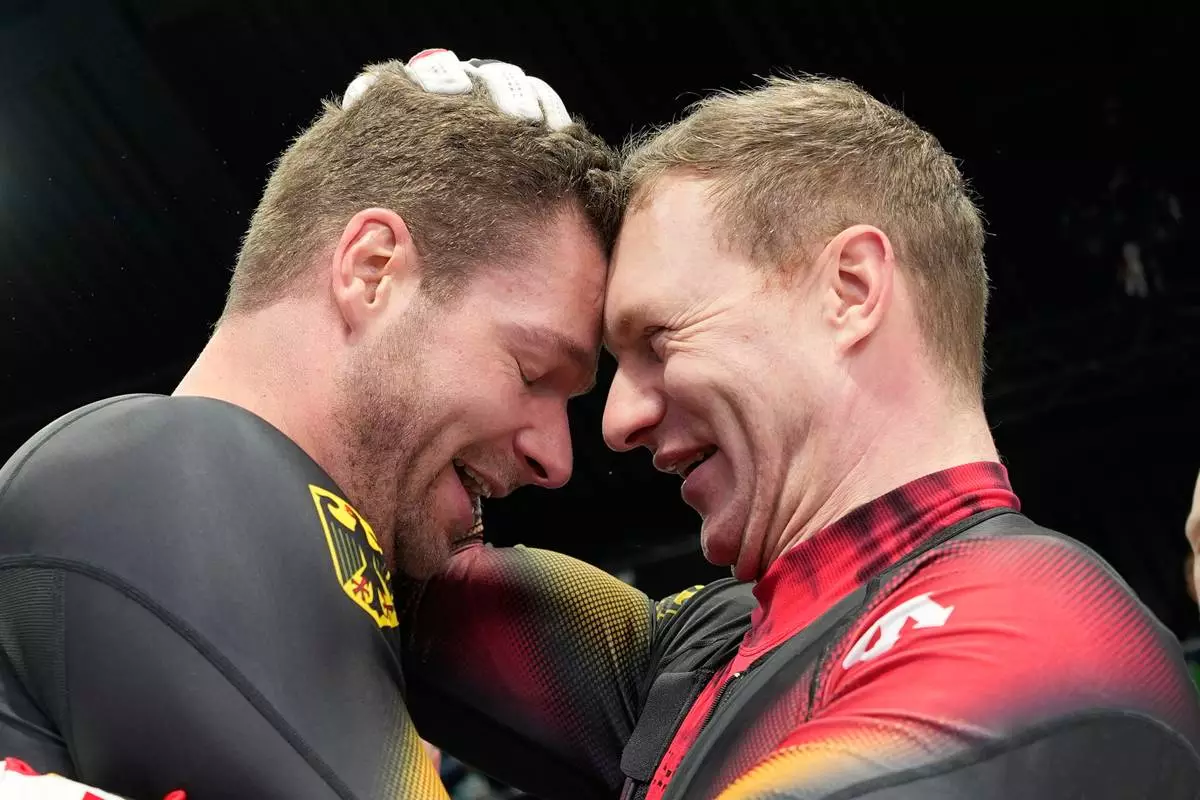Germany's gold medalists Johannes Lochner, left, and Germany's silver medalist Francesco Friedrich, right, celebrate at the finish after the four man bobsled competition at the 2026 Winter Olympics, in Cortina d'Ampezzo, Italy, Sunday, Feb. 22, 2026. (AP Photo/Alessandra Tarantino)