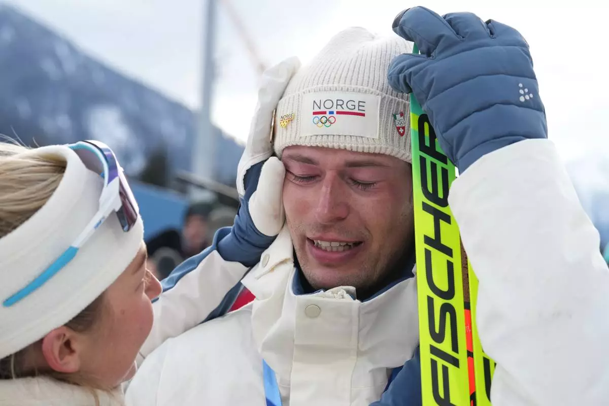 ADDS NAME OF TEAMMATE - Sturla Holm Laegreid, of Norway, reacts after he won bronze as teammate Ingrid Landmark Tandrevold comforts him after the men's 20-kilometer individual biathlon race at the 2026 Winter Olympics in Anterselva, Italy, Tuesday, Feb. 10, 2026. (AP Photo/Andrew Medichini)