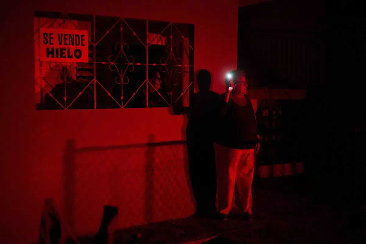 FILE - A woman holds up a cell phone flashlight as she chats with a friend during a scheduled power outage as part of energy rationing in Santa Cruz del Norte, home to one of Cuba's largest thermoelectric plants, Feb. 3, 2026. (AP Photo/Ramon Espinosa, File)