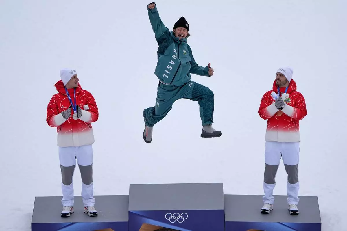 Brazil's Lucas Pinheiro Braathen, center, winner of an alpine ski, men's giant slalom race, jumps in celebration on the podium flanked by second placed Switzerland's Marco Odermatt, left, and third placed Switzerland's Loic Meillard, at the 2026 Winter Olympics, in Bormio, Italy, Saturday, Feb. 14, 2026. (AP Photo/John Locher)