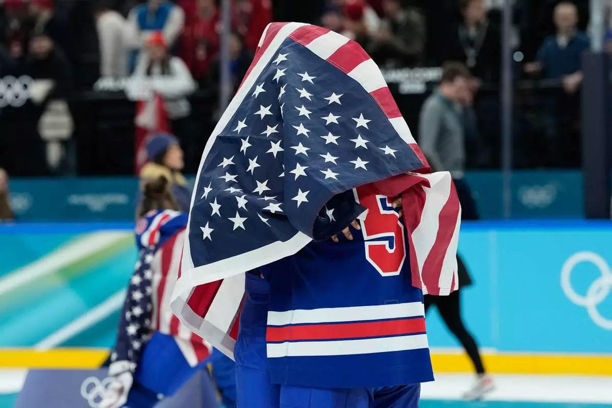 United States' Megan Keller (5), covered in the U.S. flag, gets a hug from a teammate after the United States' women's ice hockey team stand after being presented with the gold medals at the 2026 Winter Olympics, in Milan, Italy, Thursday, Feb. 19, 2026. (AP Photo/Petr David Josek)