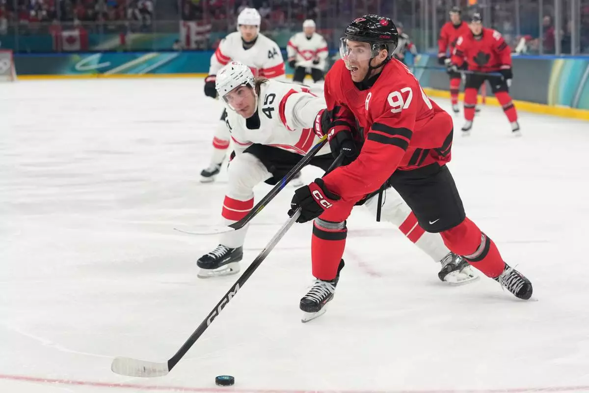 Switzerland's Michael Fora, left, challenges Canada's Connor McDavid during a preliminary round match of men's ice hockey between Canada and Switzerland at the 2026 Winter Olympics, in Milan, Italy, Friday, Feb. 13, 2026. (AP Photo/Hassan Ammar)