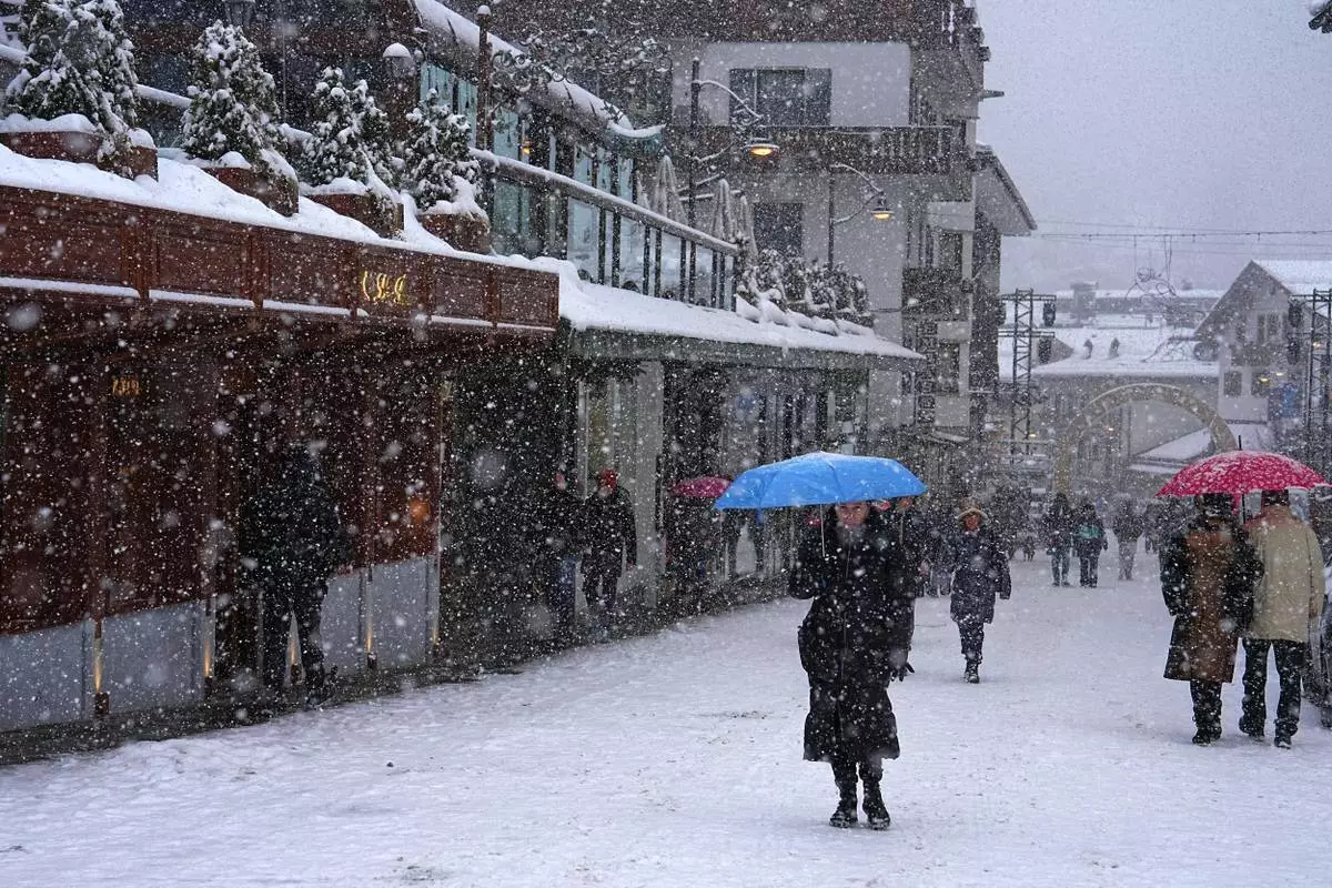 People walk along a main shopping street as snow falls ahead of the 2026 Winter Olympics, in Cortina d'Ampezzo, Italy, Tuesday, Feb. 3, 2026. (AP Photo/Fatima Shbair)