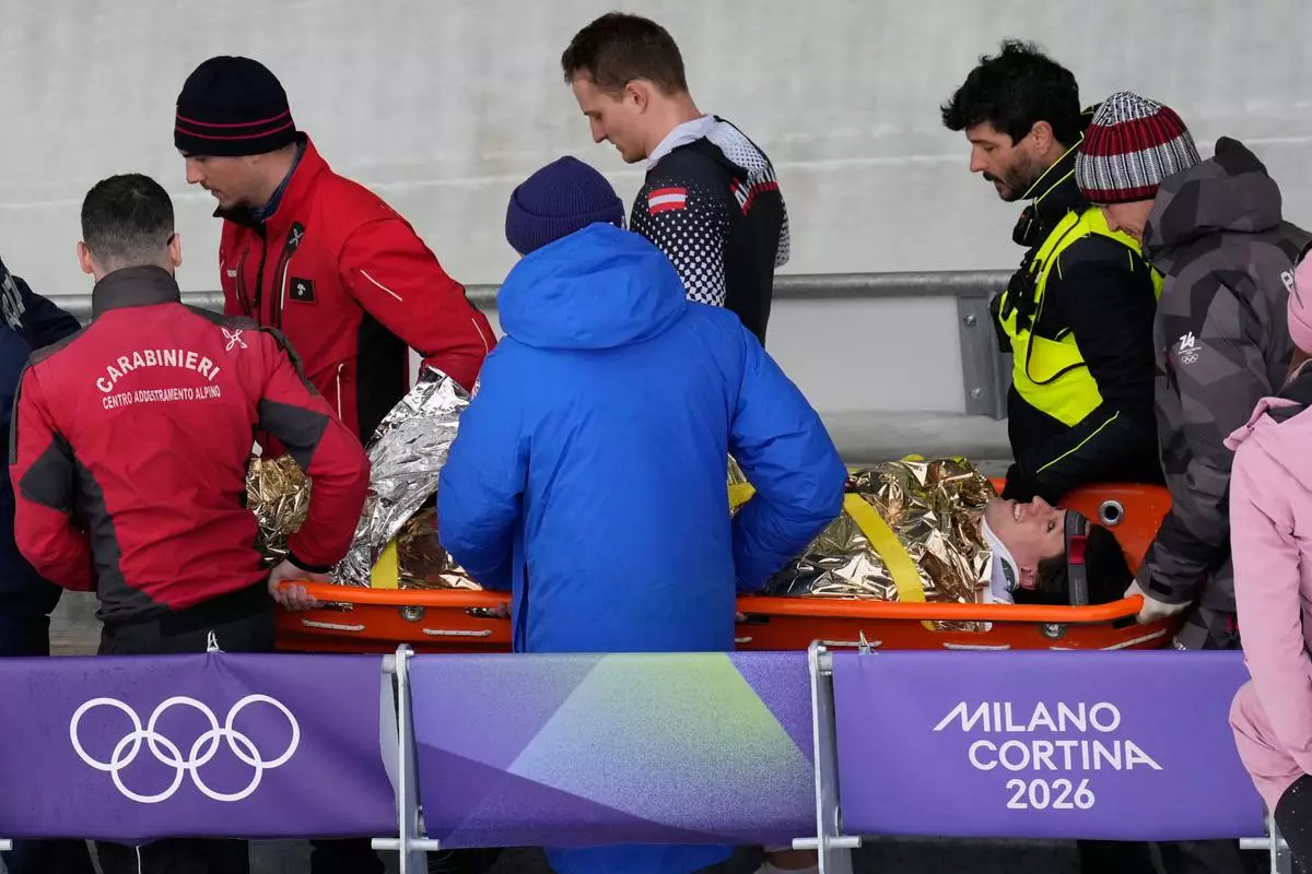 Team members and rescue workers carry an injured athlete after Austria's team Jakob Mandlbauer, Daniel Bertschler, Sebastian Mitterer and Daiyehan Nichols-Bardi crashed during a four man bobsled run at the 2026 Winter Olympics, in Cortina d'Ampezzo, Italy, Saturday, Feb. 21, 2026. (AP Photo/Aijaz Rahi)