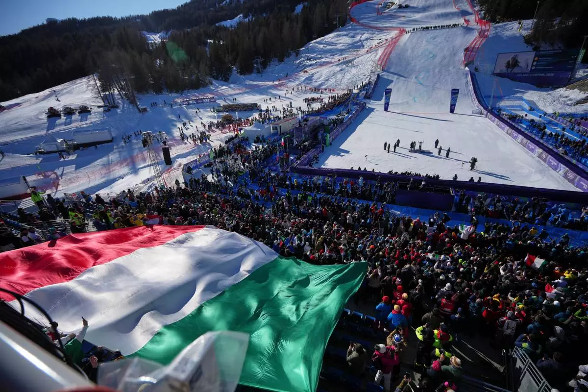 A giant Italian flag is displayed by fans during the medal ceremony where Italy's Federica Brignone won the gold medal in an alpine ski, women's giant slalom race, at the 2026 Winter Olympics, in Cortina d'Ampezzo, Italy, Sunday, Feb. 15, 2026. (AP Photo/Andy Wong)