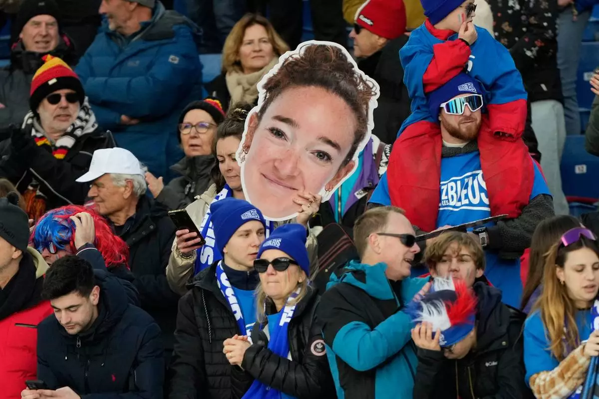 A fan holds an image of France's Lou Jeanmonnot, gold medalist in the 4X6-kilometer mixed relay biathlon race at the 2026 Winter Olympics in Anterselva, Italy, Sunday, Feb. 8, 2026. (AP Photo/Mosa'ab Elshamy)