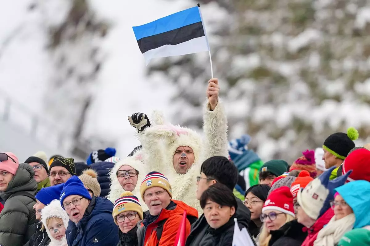 A fan waves a flag of Estonia during the ski jumping of the Nordic Combined Individual Gundersen Normal Hill/10km competition at the 2026 Winter Olympics, in Predazzo, Italy, Wednesday, Feb. 11, 2026. (AP Photo/Matthias Schrader)