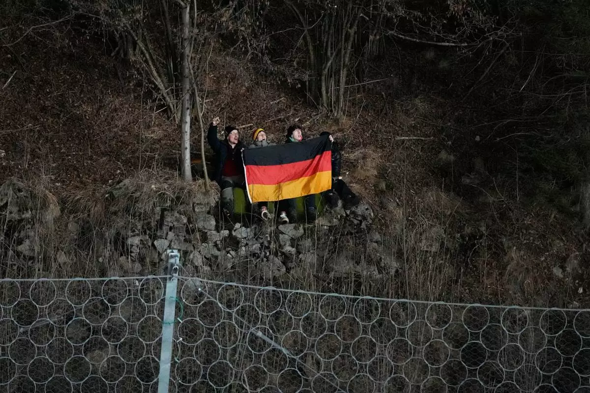 Germany fans cheer on their team from a slope overlooking the venue during the ski jumping men's super team competition at the 2026 Winter Olympics, in Predazzo, Italy, Monday, Feb. 16, 2026. (AP Photo/Armando Franca)